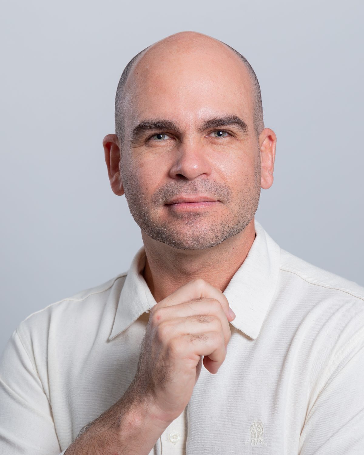 Felipe Lapa, de camisa clara, com a mão no queixo, olhando para a câmera